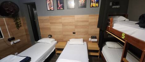 A room with three single beds, a wooden headboard, a wall-mounted fan, and several framed pictures.