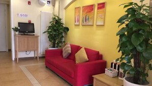 A red sofa, a television on a stand, a potted plant, and a small table with a basket. - Homeinn Hotel (Beijing Dinghui Bridge Wuluju Subway Station) (Beijing)