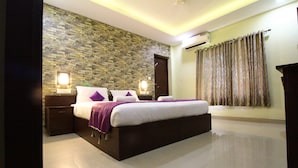 A modern bedroom with a stone wall, a large bed with purple bedding, and a nightstand with a lamp. - North Centre (Kanayannur)
