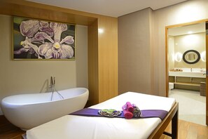 A bathroom with a bathtub, a large mirror, and a bed with towels. - Surya Hotel & Cottages Prigen (Prigen)