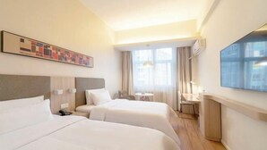 Habitación de hotel con dos camas, un escritorio, una silla y un ventanal grande.