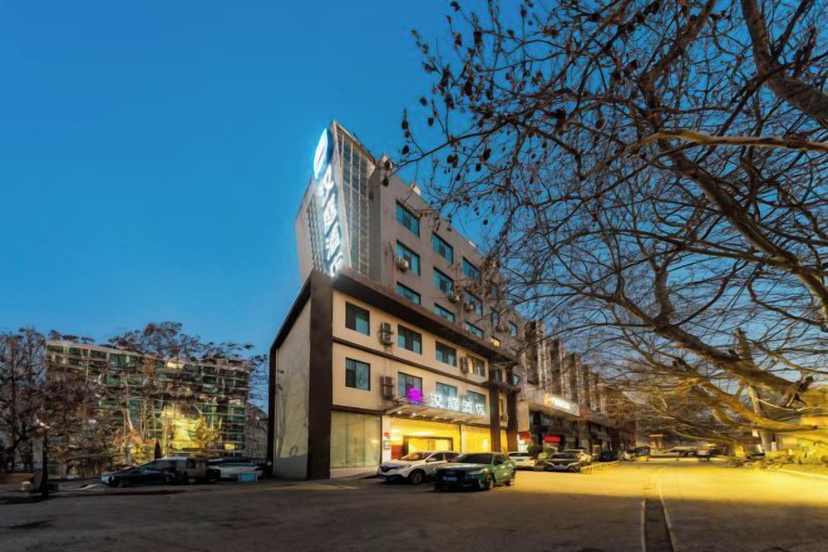 A multi-story hotel with a modern design, located in an urban setting with trees and parked cars.