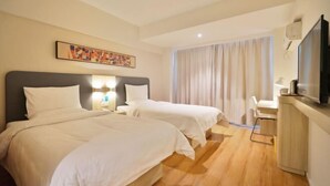 Habitación de hotel con dos camas, un escritorio, televisión y una ventana con cortinas.