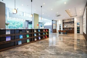 Un hall d’hôtel avec un sol en marbre, un comptoir d’accueil doté d’une cloison en verre et un espace détente avec des tables et des chaises.