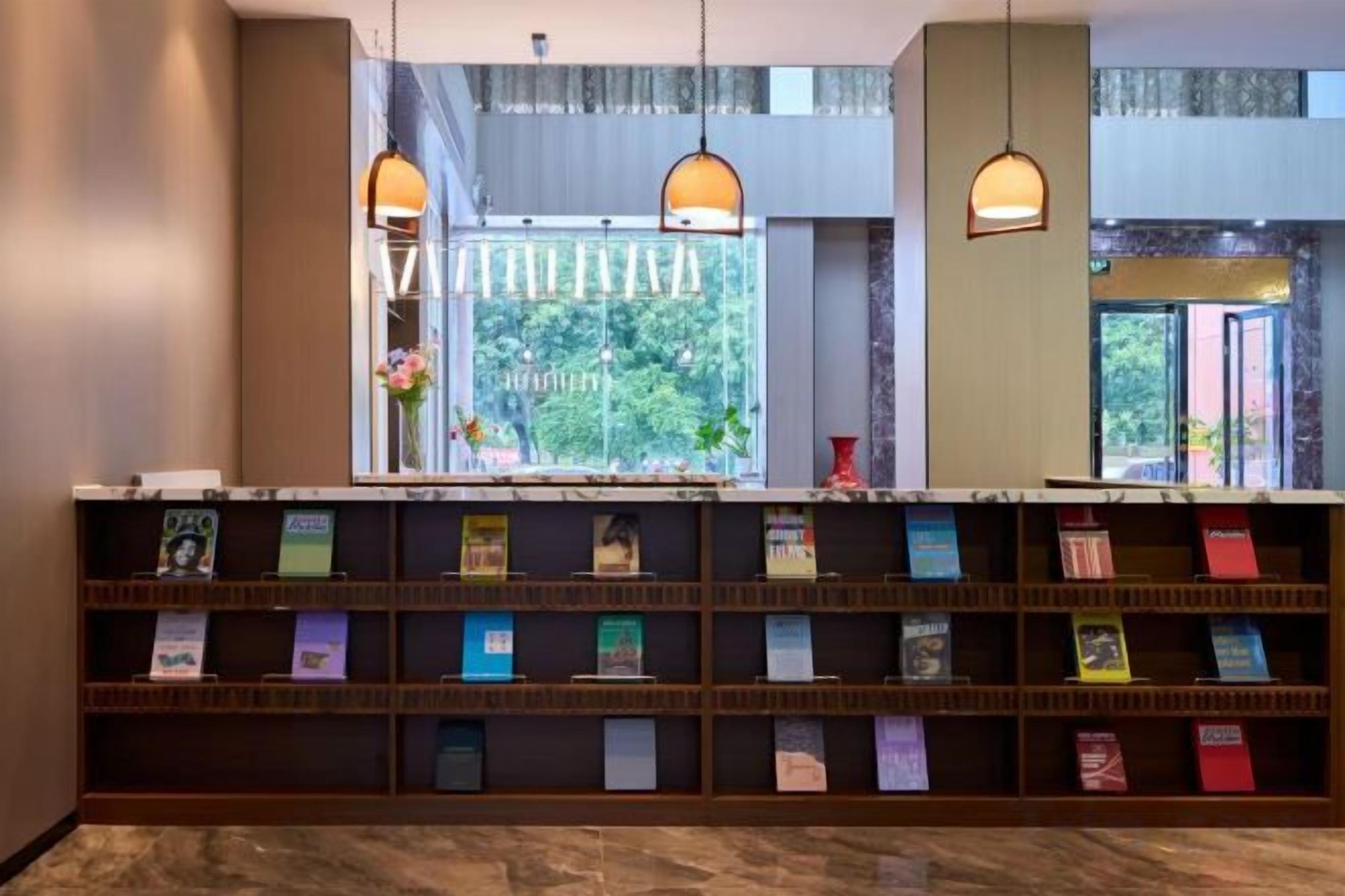 Un'area reception con una libreria, due lampade a sospensione e una finestra vista verde.