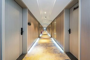 Un couloir d’hôtel avec des portes des deux côtés, un sol recouvert de moquette et un plafond doté d’un éclairage encastré.