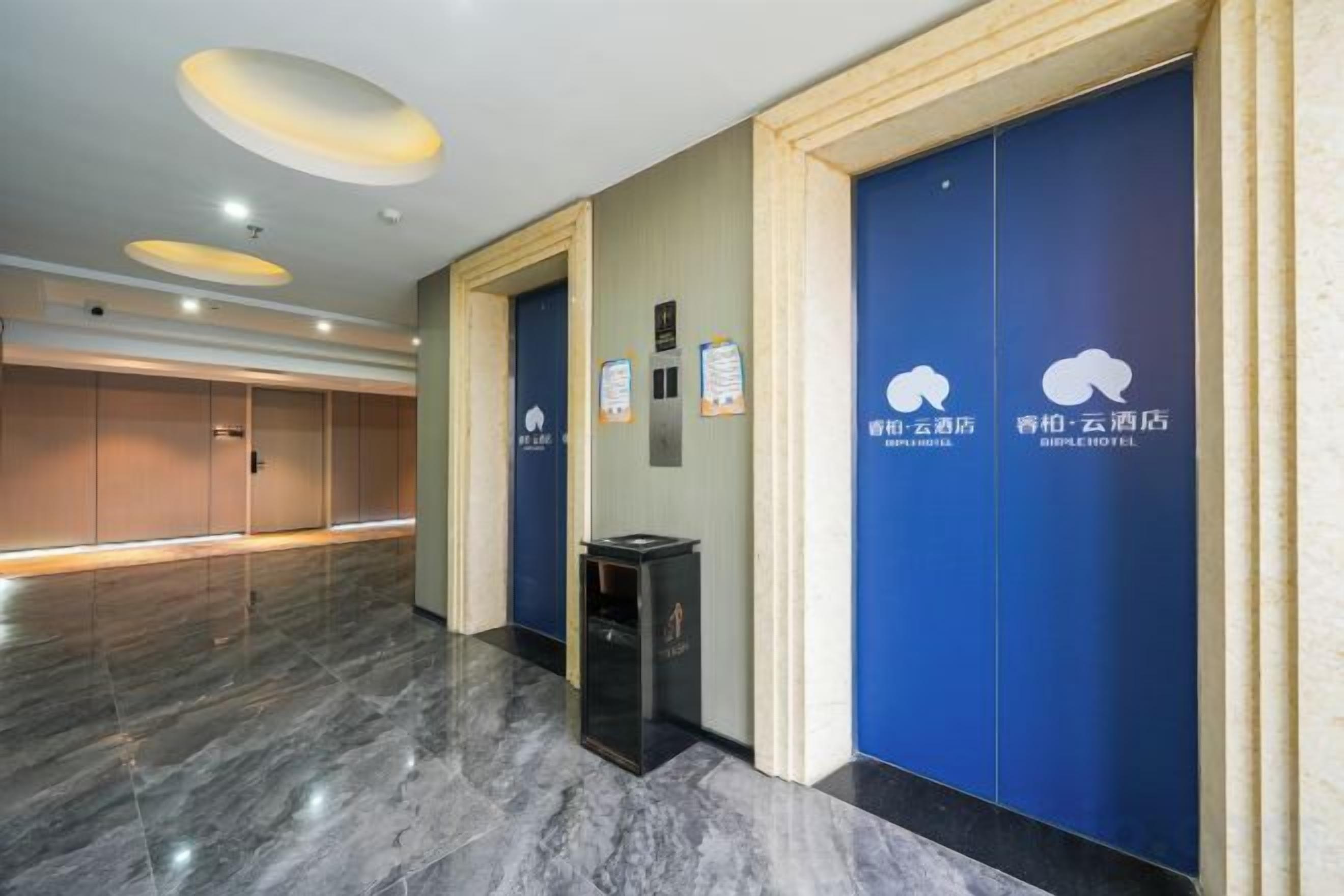 A hotel lobby with a marble floor, blue doors, and a trash bin.