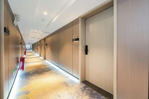Hotelgang med døre mærket med værelsesnumre, et tæppe gulv og et moderne loftdesign.