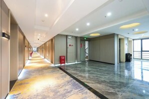 Un pasillo de hotel con piso de mármol, un extintor rojo y una escalera que sube a un nivel superior.