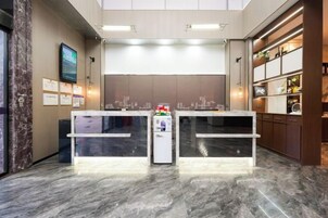 Zona de recepción con piso de mármol, mostrador de recepción, pantalla digital y televisor montado en la pared.