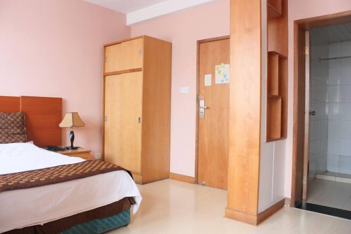 A hotel room with a bed, a nightstand, a wooden wardrobe, and a door leading to a bathroom.