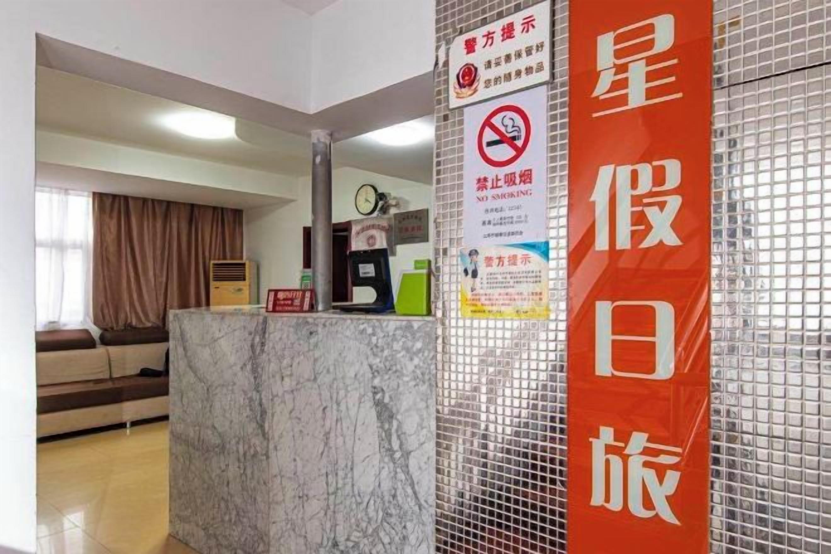 Zona de recepción de hotel con mostrador de mármol, un letrero vertical rojo con caracteres chinos y un cartel de prohibido fumar.