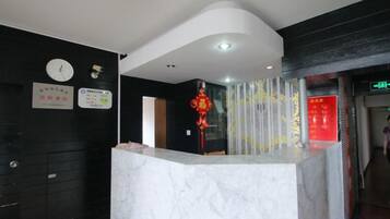 A hotel reception area with a marble counter, black walls, and a clock.