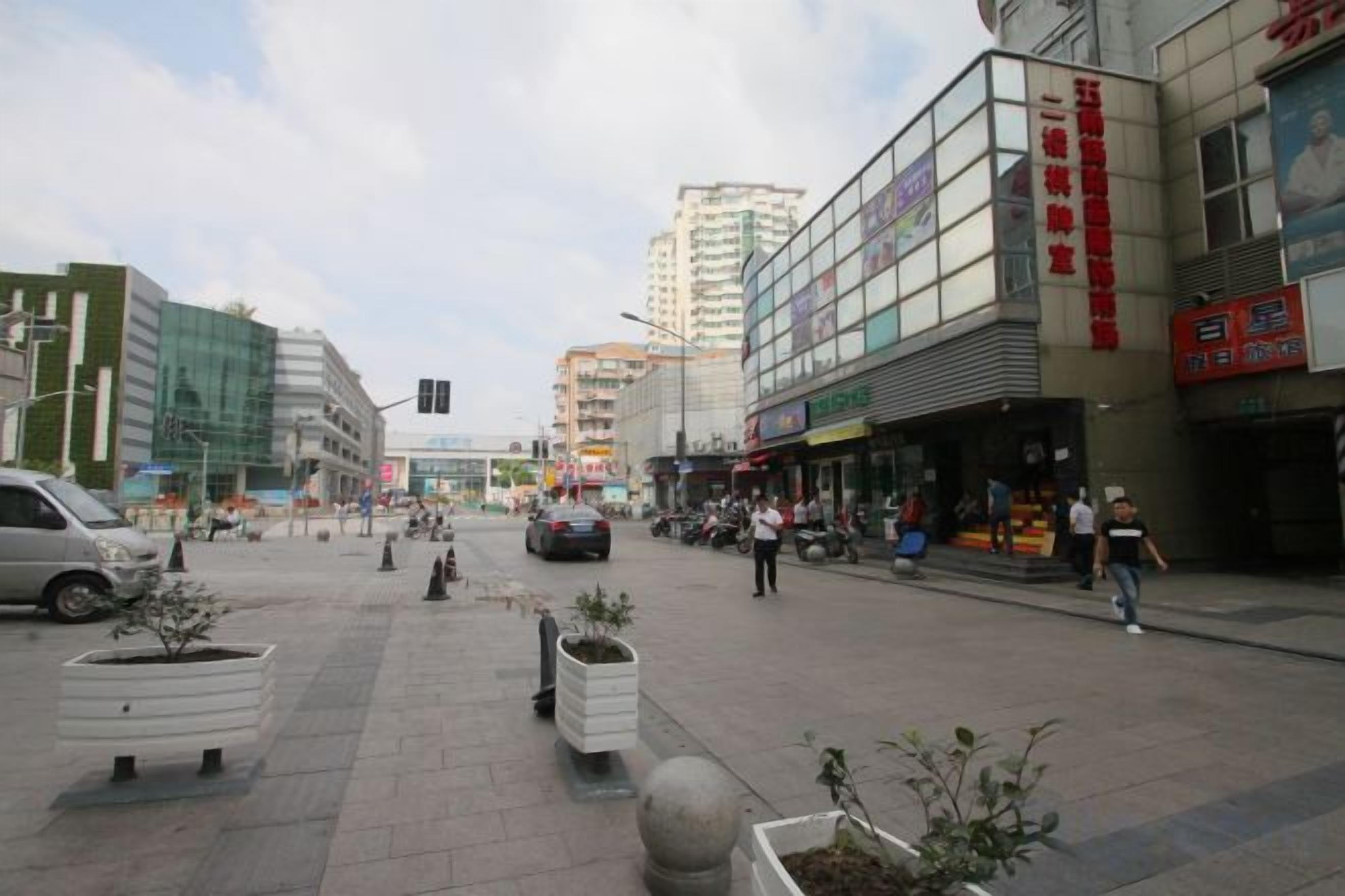 Una plaza urbana con edificios modernos, una zona peatonal y macetas con plantas.