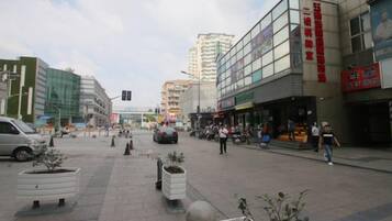 Una plaza urbana con edificios modernos, una zona peatonal y macetas con plantas.