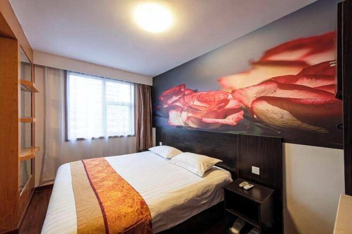 A hotel room with a large bed, a nightstand, a wall-mounted TV, and a window with curtains.
