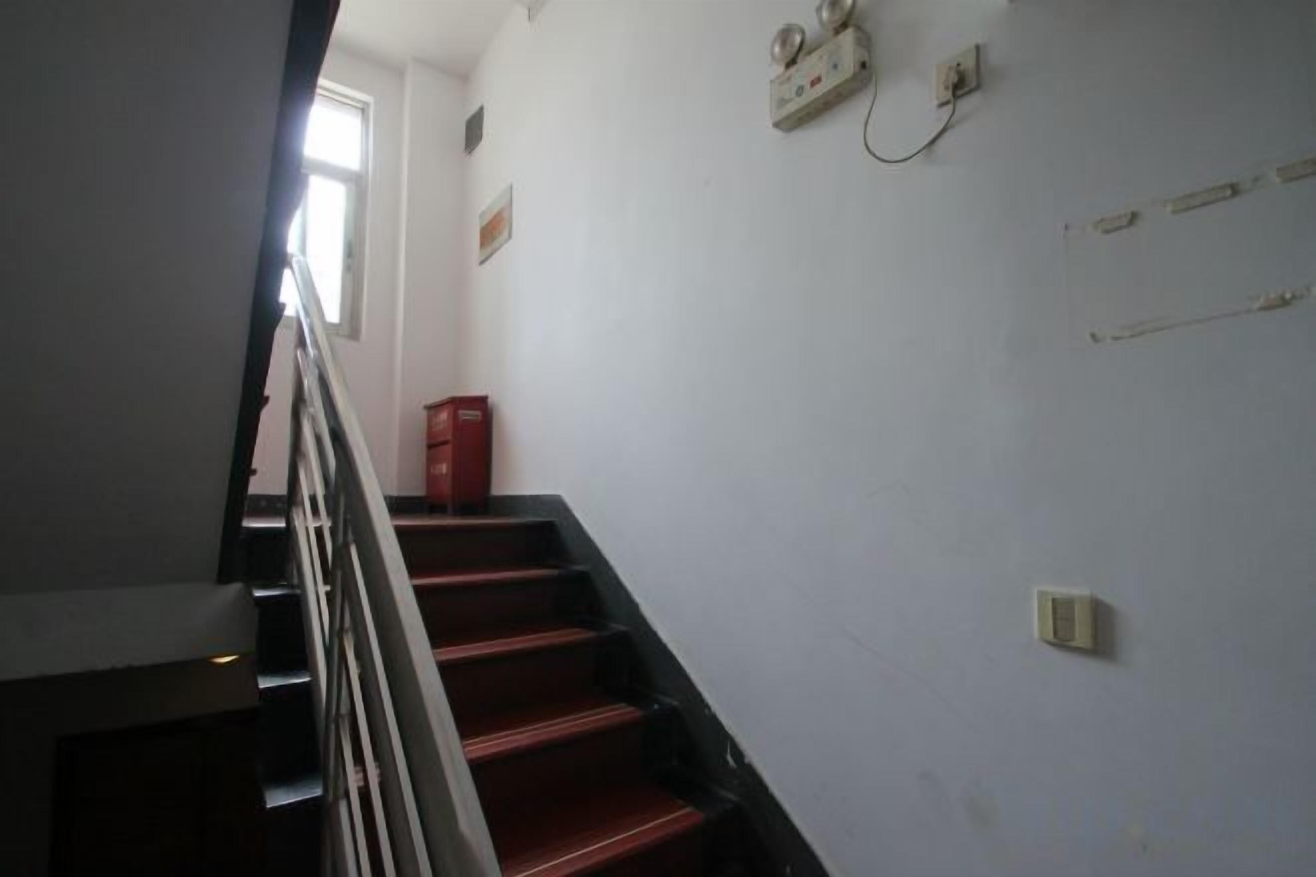 A staircase with a handrail, a red fire extinguisher, and a wall-mounted electrical outlet.
