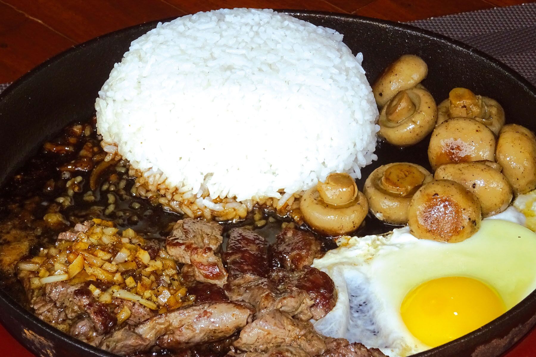 Uma refeição com arroz, cogumelos, carne e um ovo.