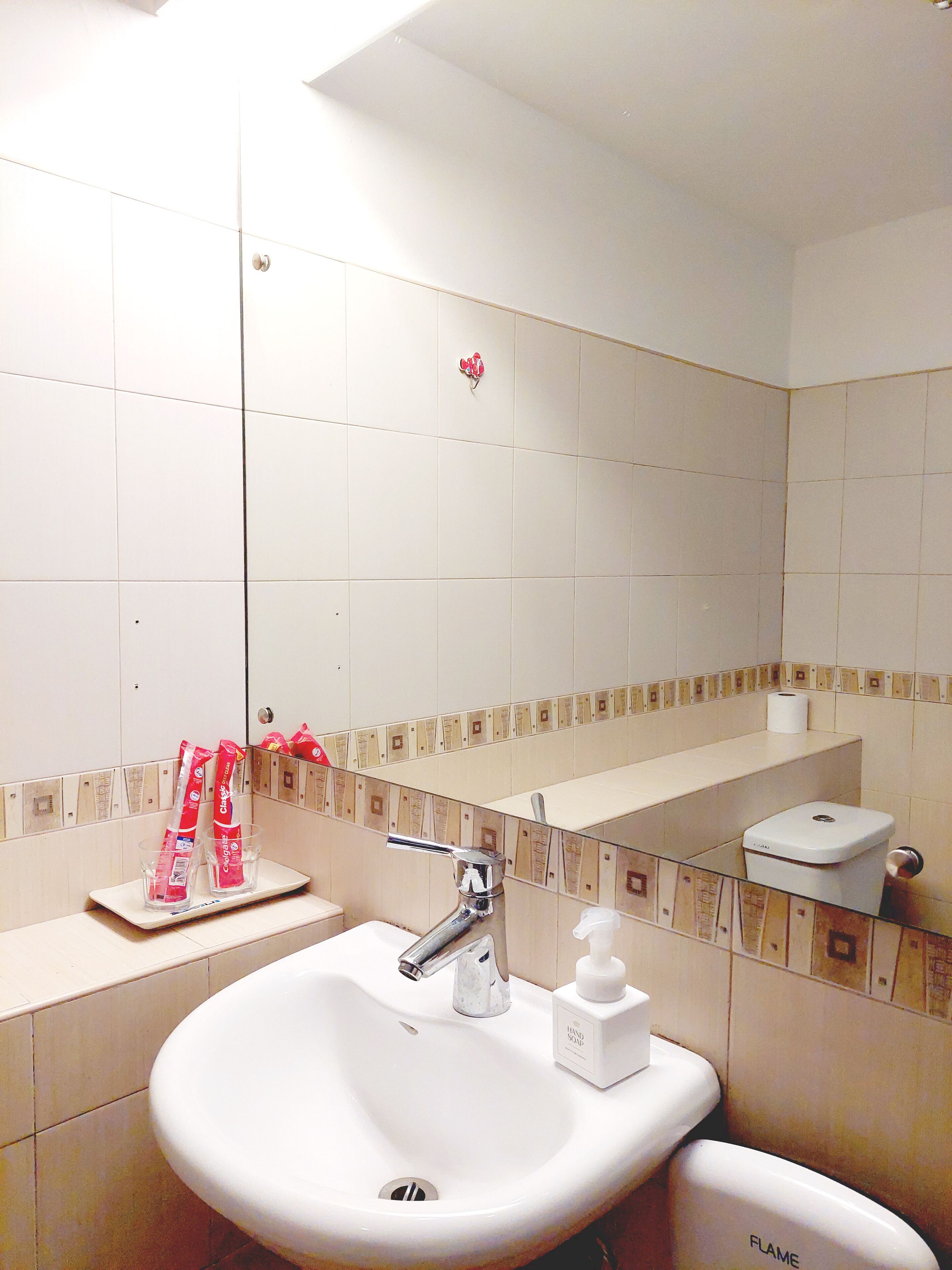 A bathroom with a sink, mirror, toilet, and a shelf with toiletries.
