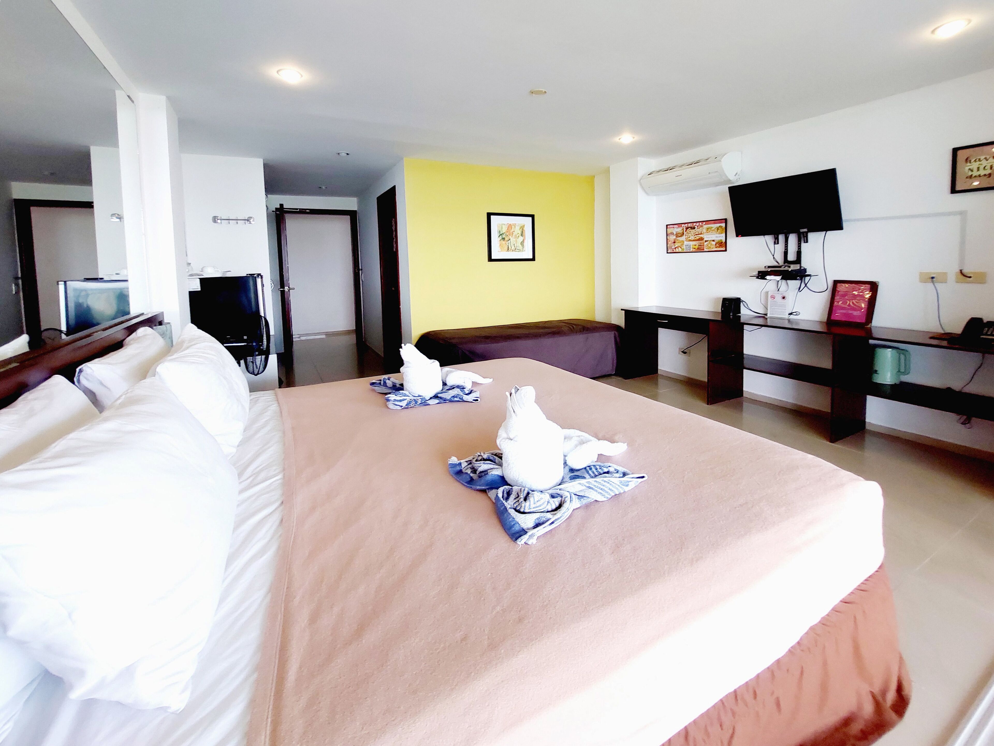 Habitación de hotel con cama, escritorio con computadora, televisor y aire acondicionado instalado en la pared.