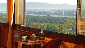 A wooden table with a vase of flowers, a lamp, and a framed picture in a room with a large window overlooking a city and mountains. - Bohol Vantage Resort (Dauis)