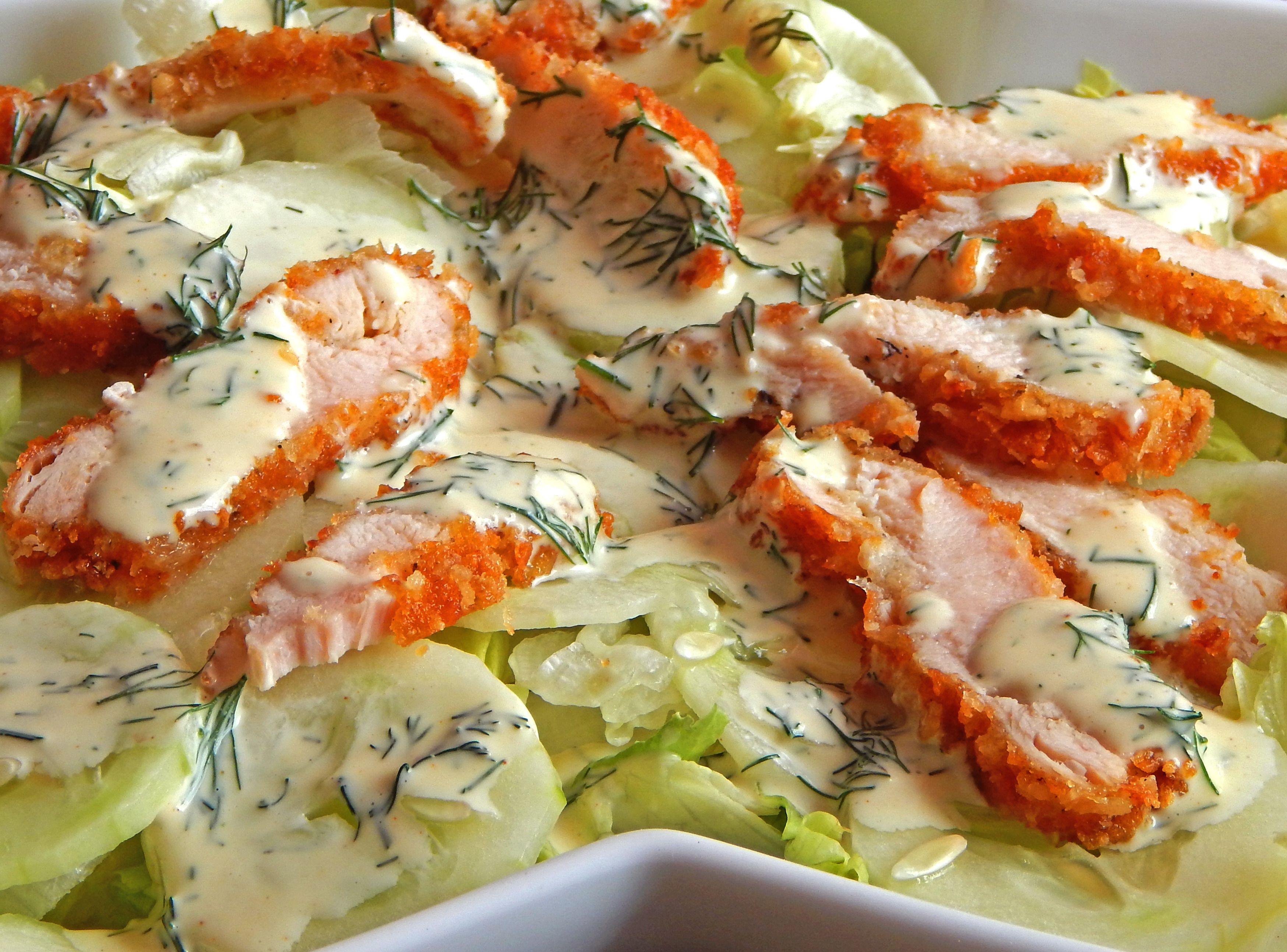 A dish with breaded chicken slices, lettuce, and a creamy sauce, garnished with dill.