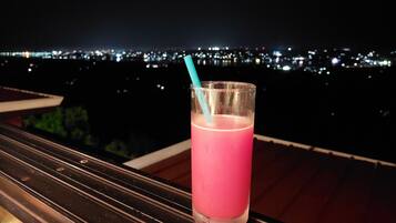 A glass of pink drink with a straw on a balcony with a city view at night.