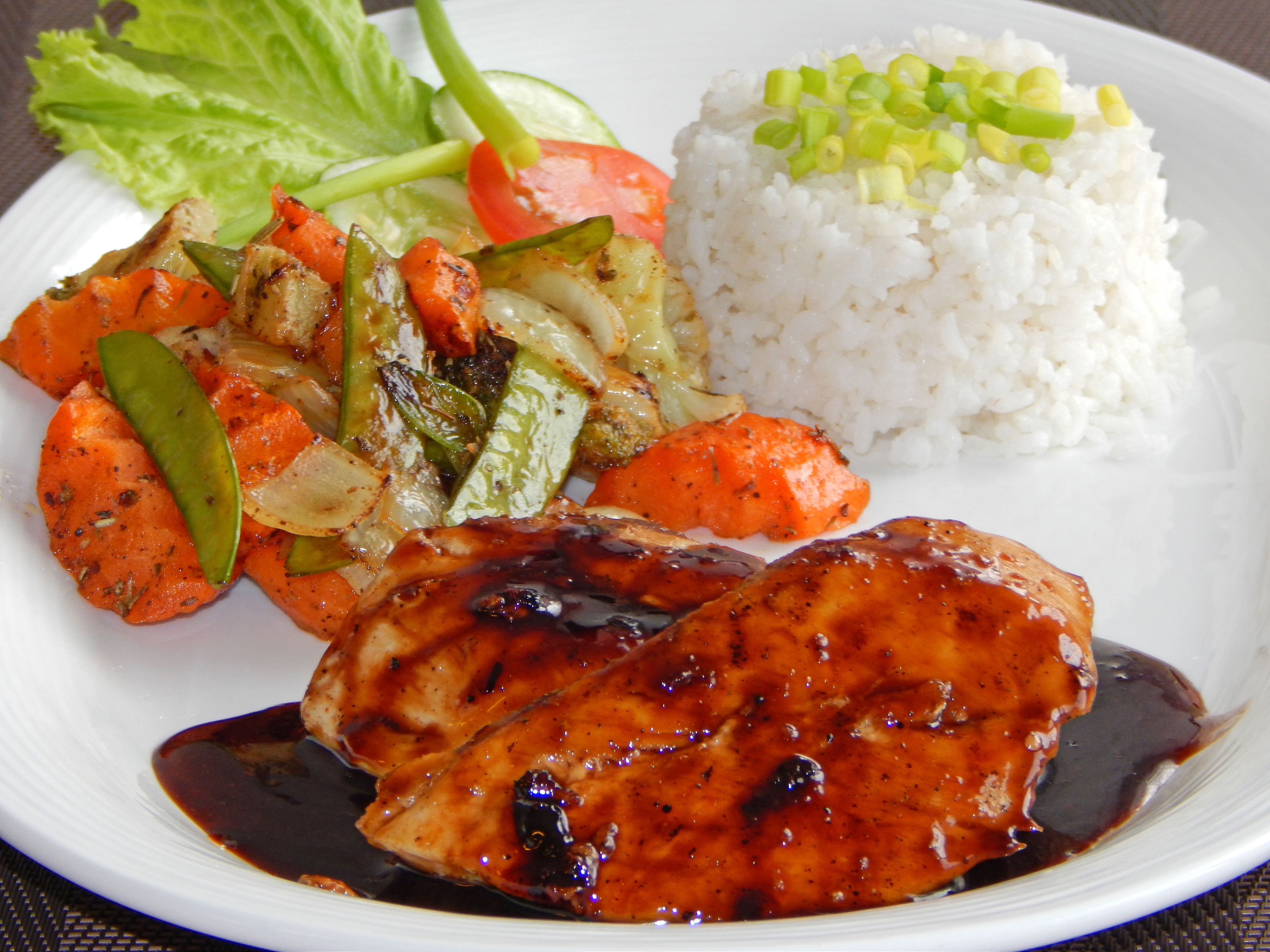 A plate of food including rice, vegetables, and a piece of meat with sauce.