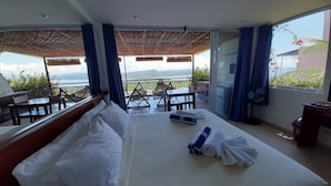 A hotel room with a bed, a table, chairs, and a balcony with a view. - Bohol Vantage Resort (Dauis)