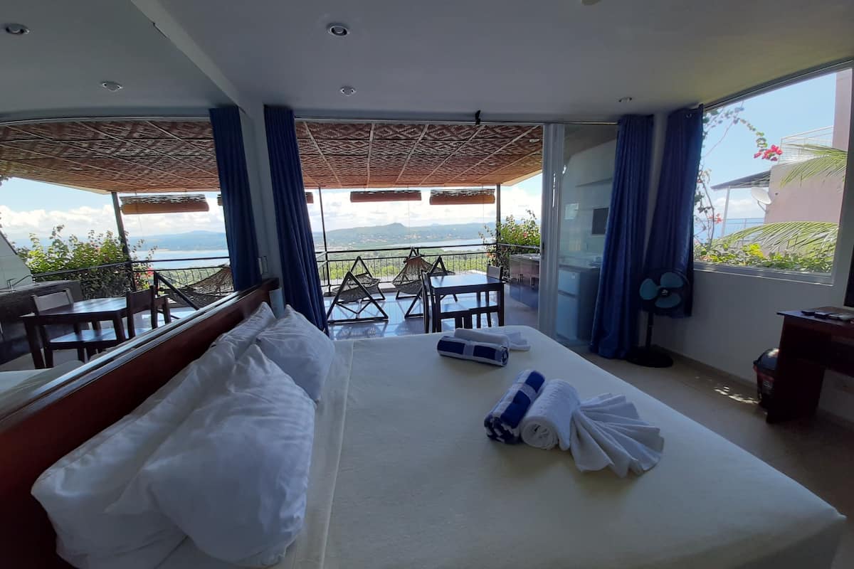 A hotel room with a bed, a table, chairs, and a balcony with a view.