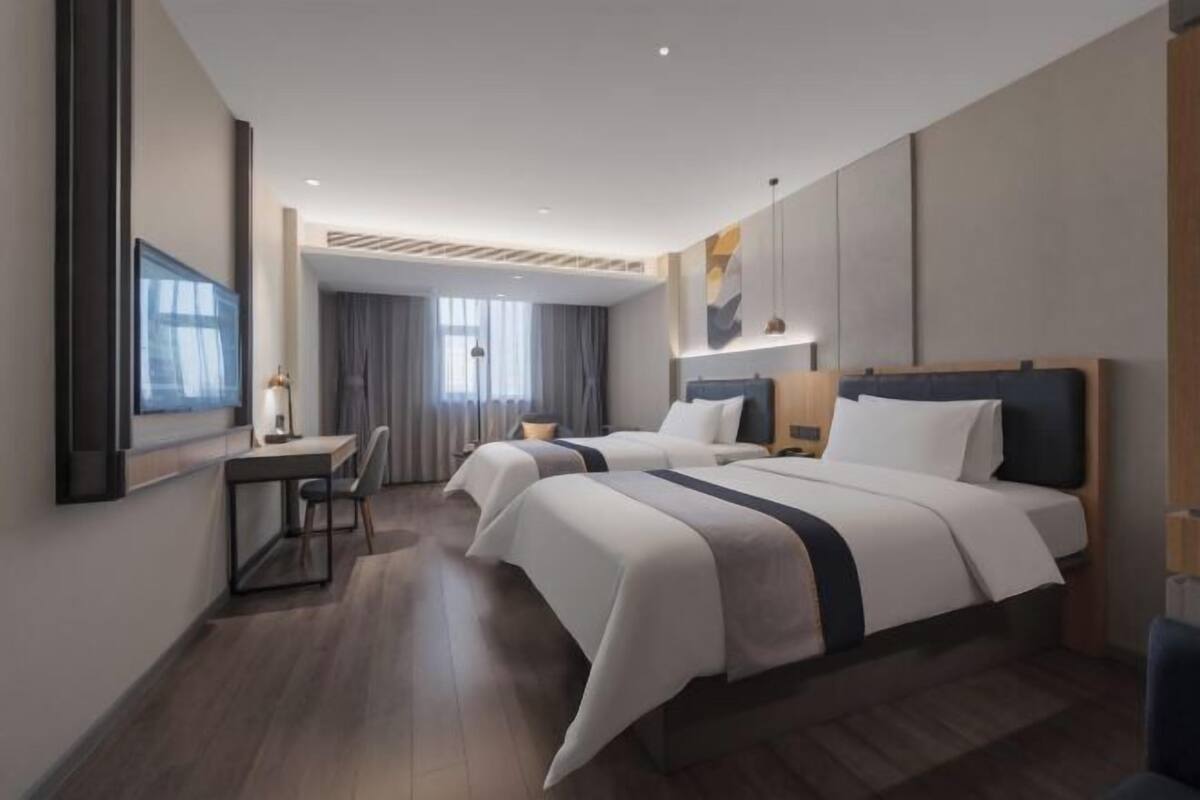 A modern hotel room with two beds, a desk, and a large window.