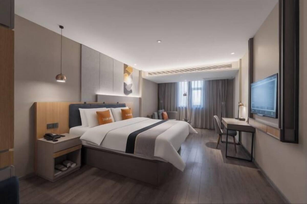 A modern hotel room with a bed, bedside table, desk, chair, and a TV mounted on the wall.