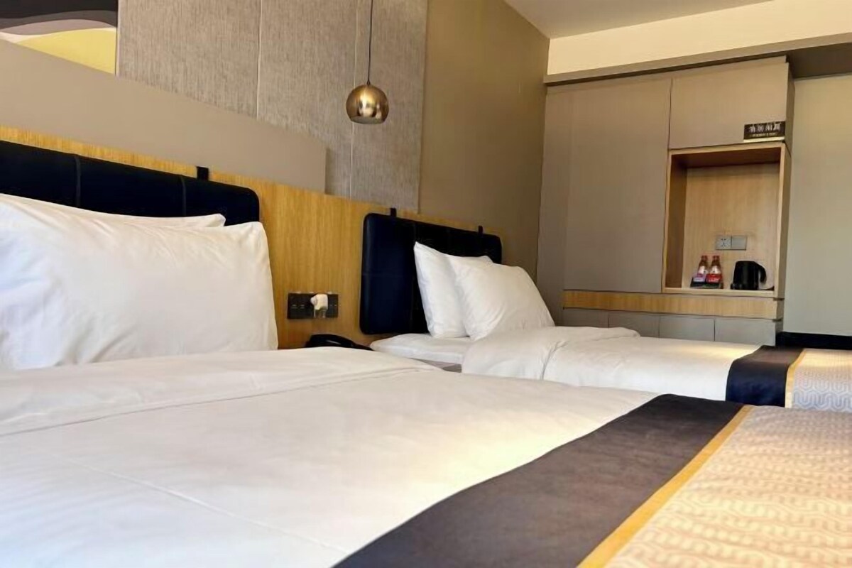 A hotel room with two beds, a wooden headboard, a bedside table with a lamp, and a mirror.