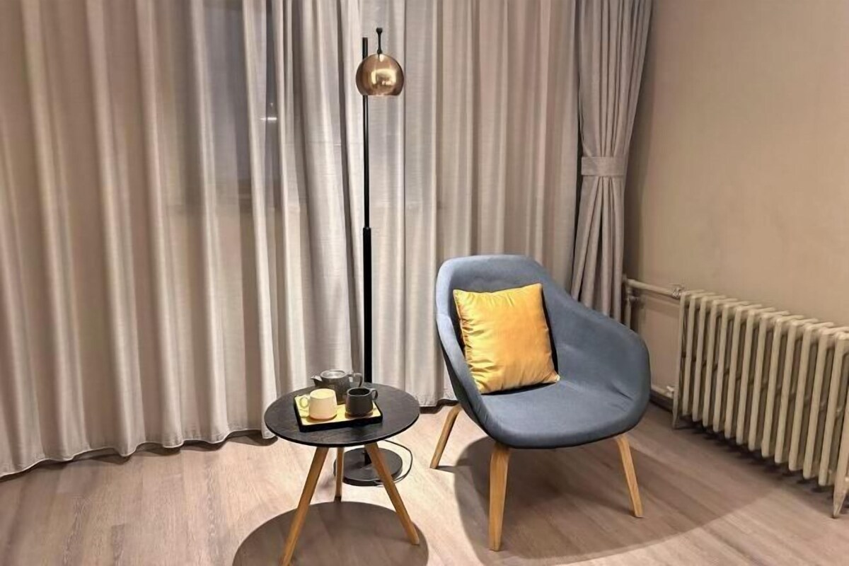 A modern room with a blue chair, a small table with a cup and saucer, a floor lamp, and a radiator.