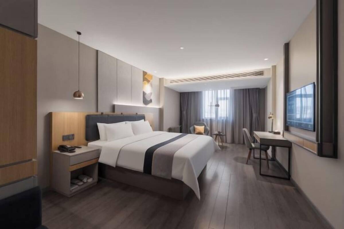 A modern hotel room with a large bed, a desk, a chair, a TV, and a wardrobe.