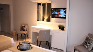 A hotel room with a bed, a desk with a chair, a television, and a small plant. - Hotel Cariatis (Nea Propontida)