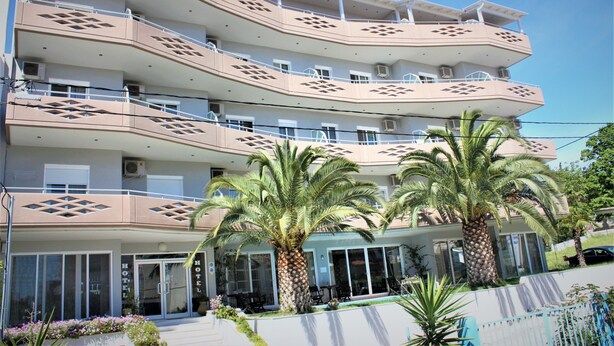 A multi-story hotel with balconies, palm trees, and a swimming pool. - Hotel Cariatis (Nea Propontida)