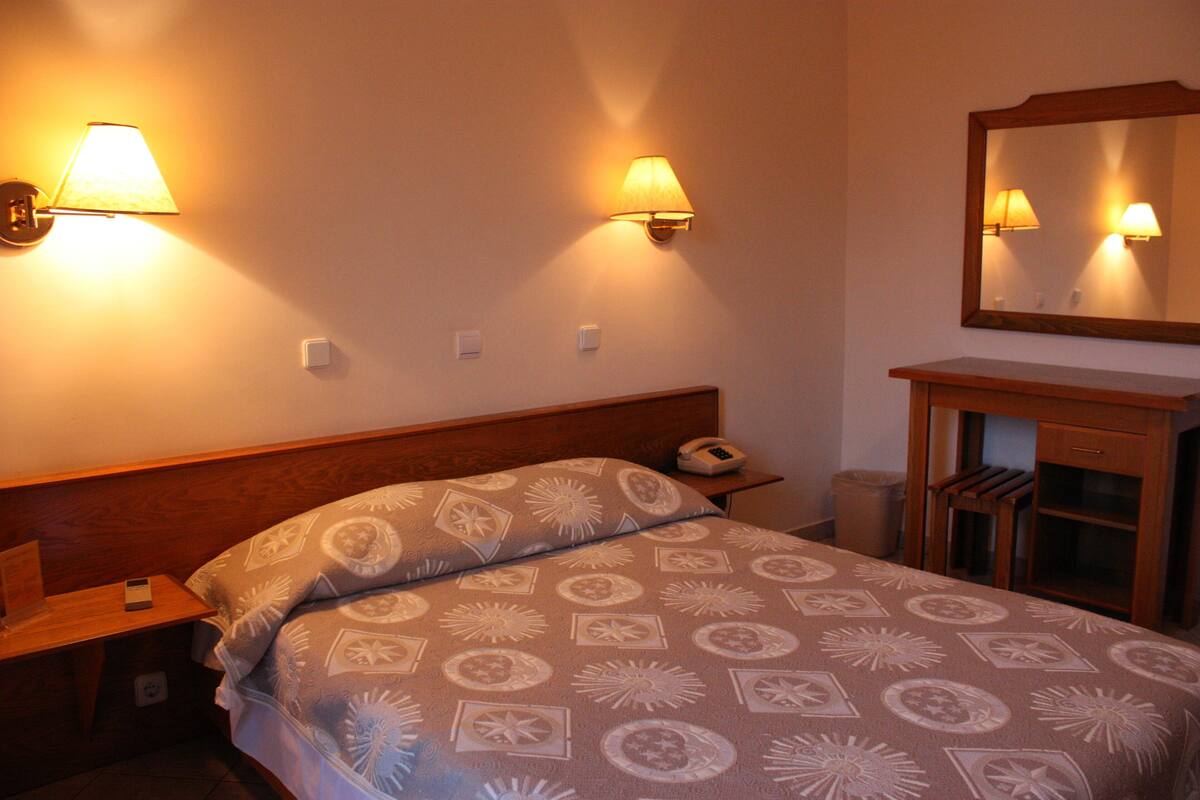 A hotel room with a bed, nightstand, lamp, and a mirror.