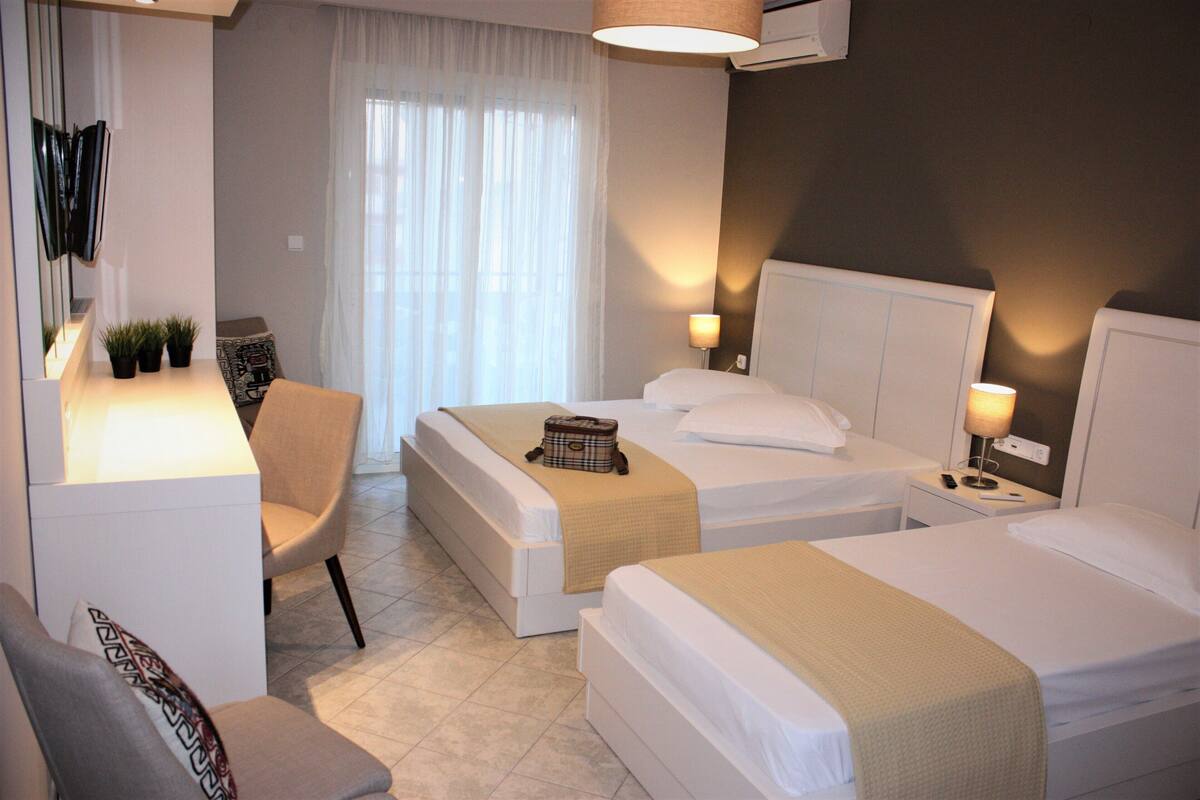 A hotel room with two beds, a chair, a desk, and a window with curtains.