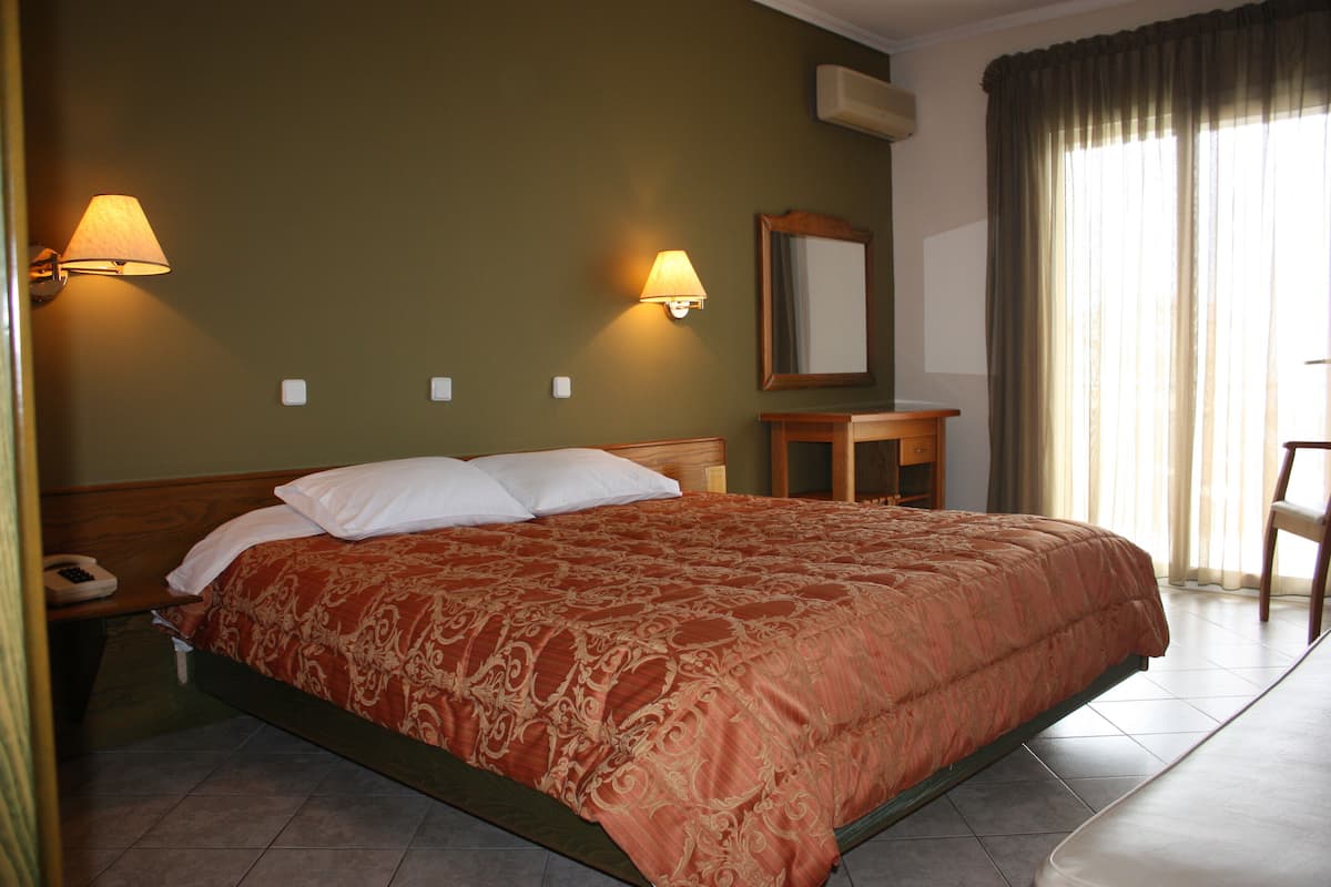 A hotel room with a large bed, two bedside lamps, a wooden nightstand, a small table, a chair, and a mirror on the wall.