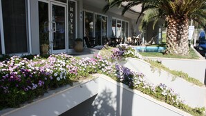A hotel entrance with a palm tree, outdoor seating, and a flower garden. - Hotel Cariatis (Nea Propontida)