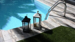 A swimming pool with a tiled edge, a metal ladder, and two lanterns on the deck. - Hotel Cariatis (Nea Propontida)