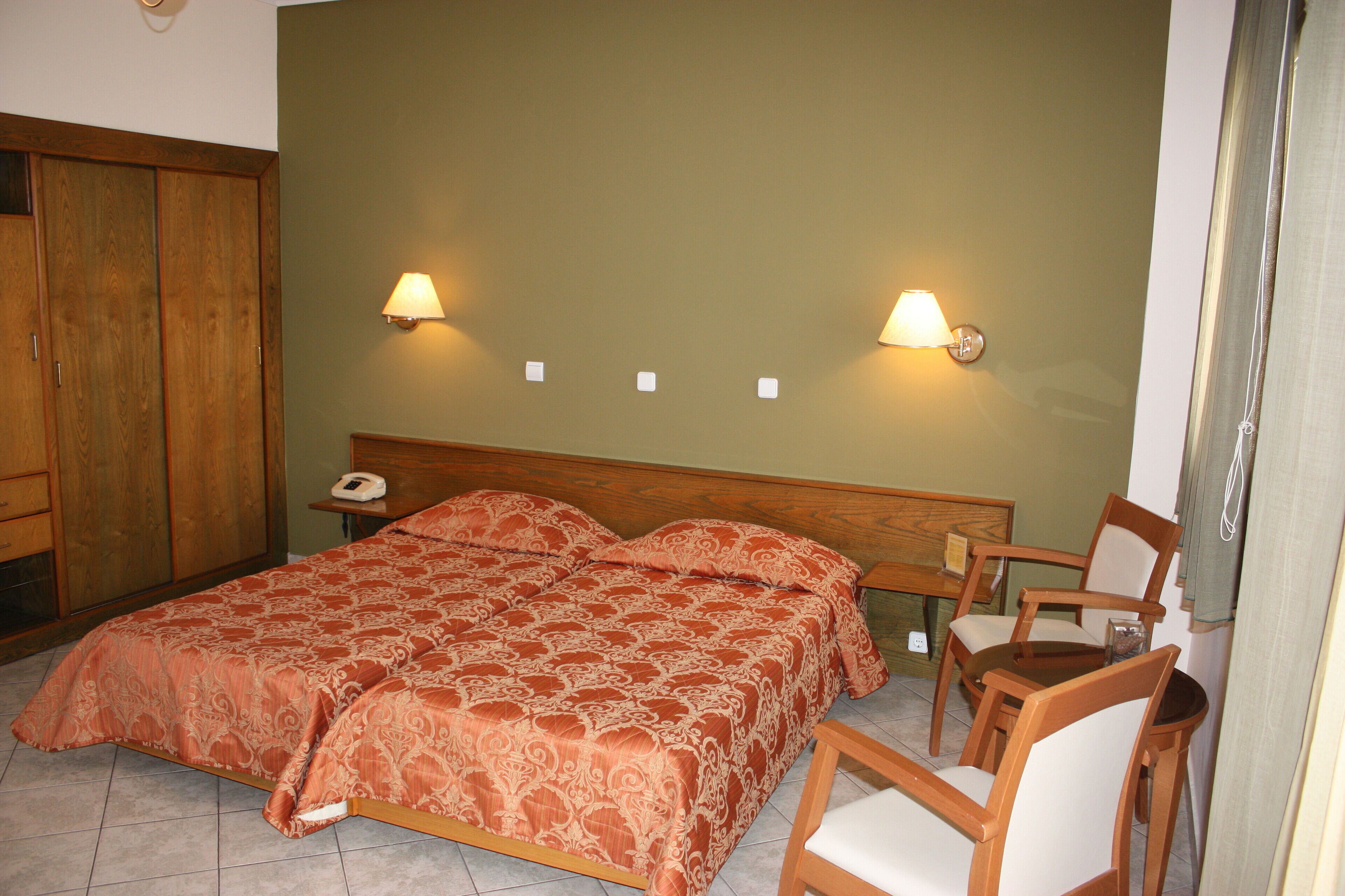 Un dormitorio con dos camas, un armario de madera, una mesita de noche con lámpara y una silla.