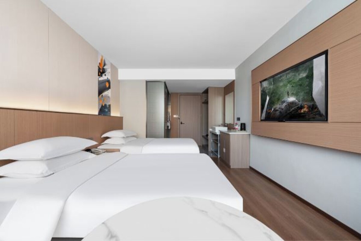 Habitación de hotel moderna con una cama grande, un televisor montado en la pared y vista a la ciudad.