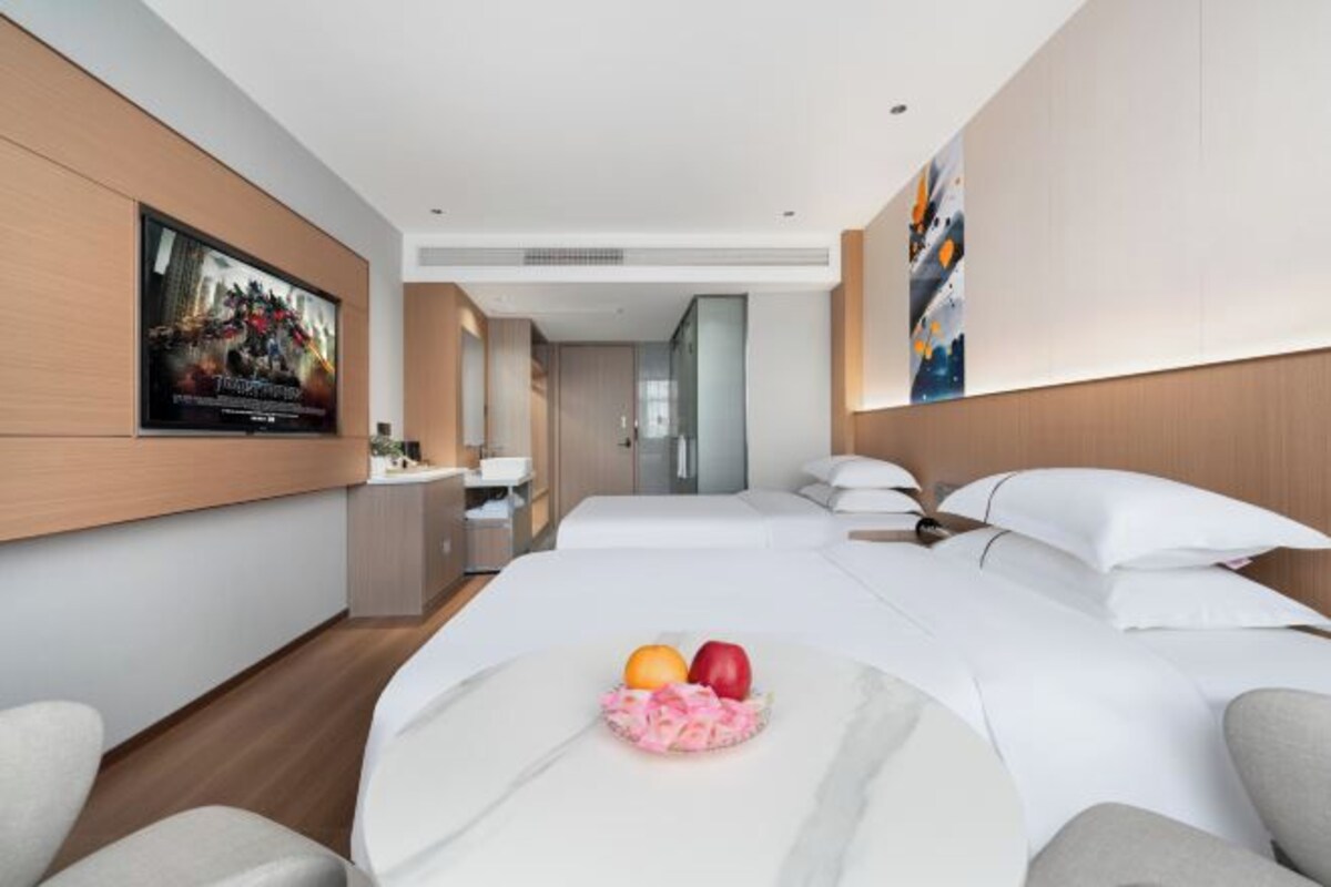 Una habitación de hotel moderna con una cama grande, un escritorio pequeño, un televisor y un frutero sobre la cama.