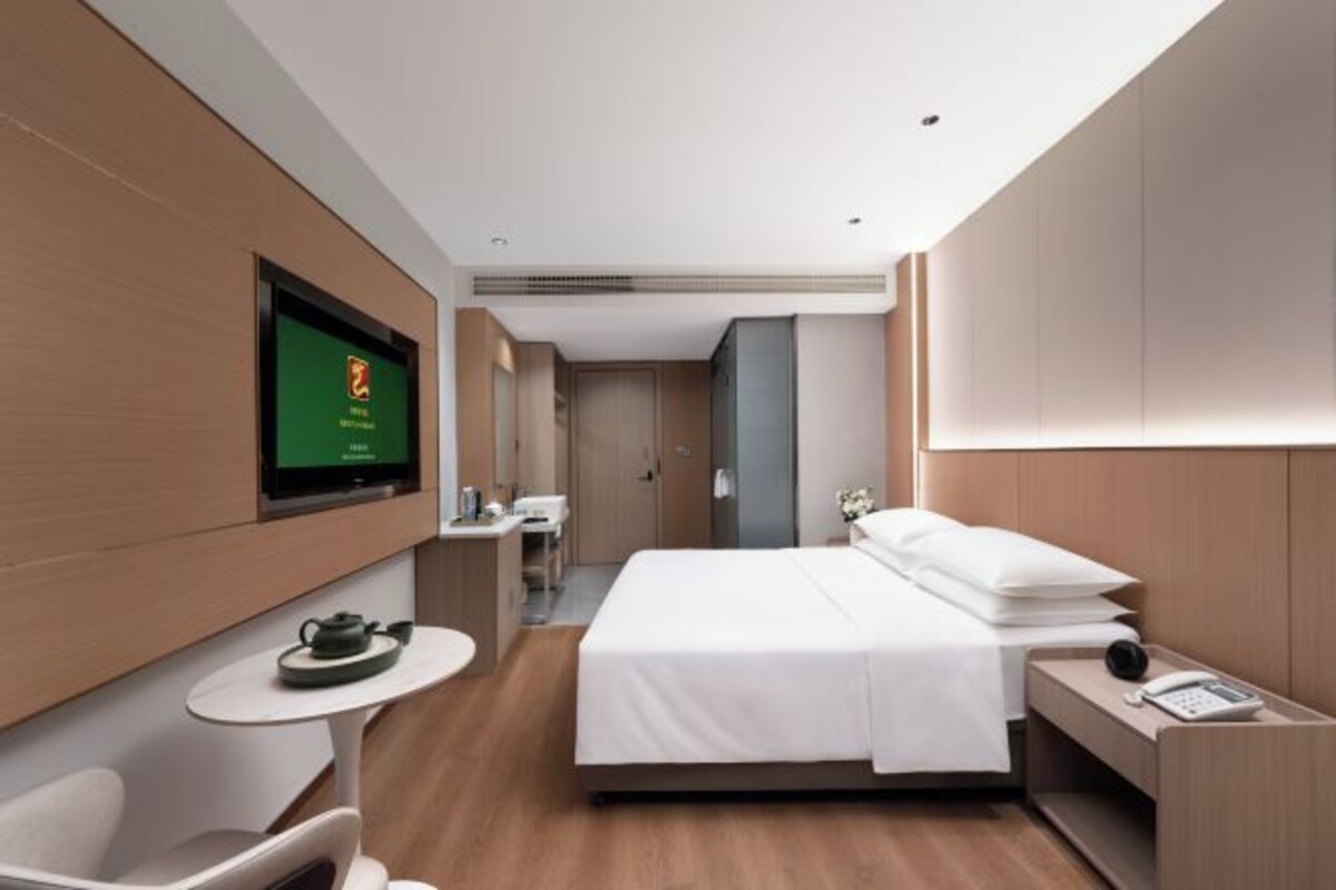 Una habitación de hotel moderna con cama, mesita de noche, televisión y un pequeño rincón de descanso.