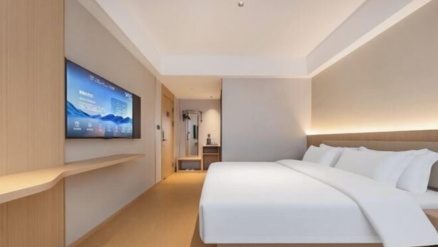 A modern hotel room with a large bed, a flat-screen TV mounted on the wall, and a wooden bedside table. - Winchi Joyu Hostel (Wenzhou)