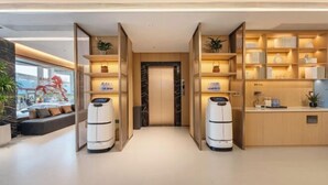 A modern hotel lobby with a central elevator, open shelving with books and decor, and a reception desk. - Winchi Joyu Hostel (Wenzhou)
