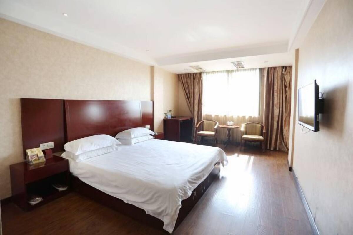 A hotel room with a large bed, a bedside table, a TV, a chair, and a small table.