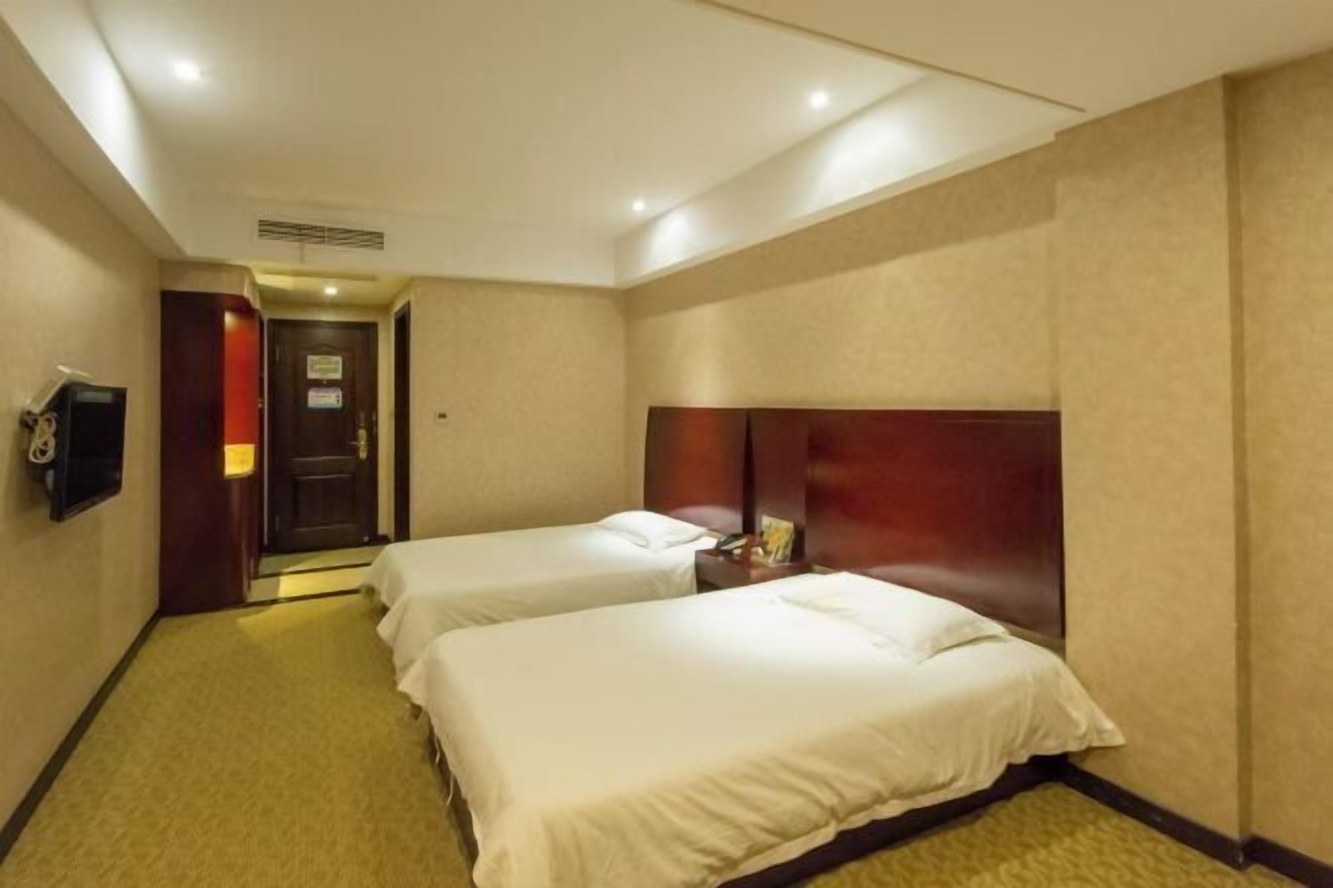 Habitación de hotel con dos camas, un televisor y una puerta que da a otra habitación.